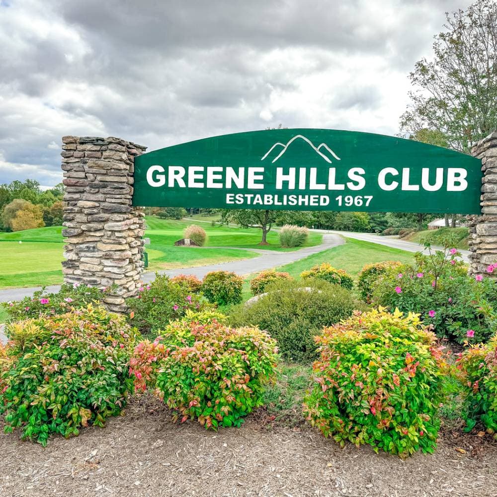The Greene Hills Club stone entrance sign reading 'Established 1967' with flowering seasonal plantings.
