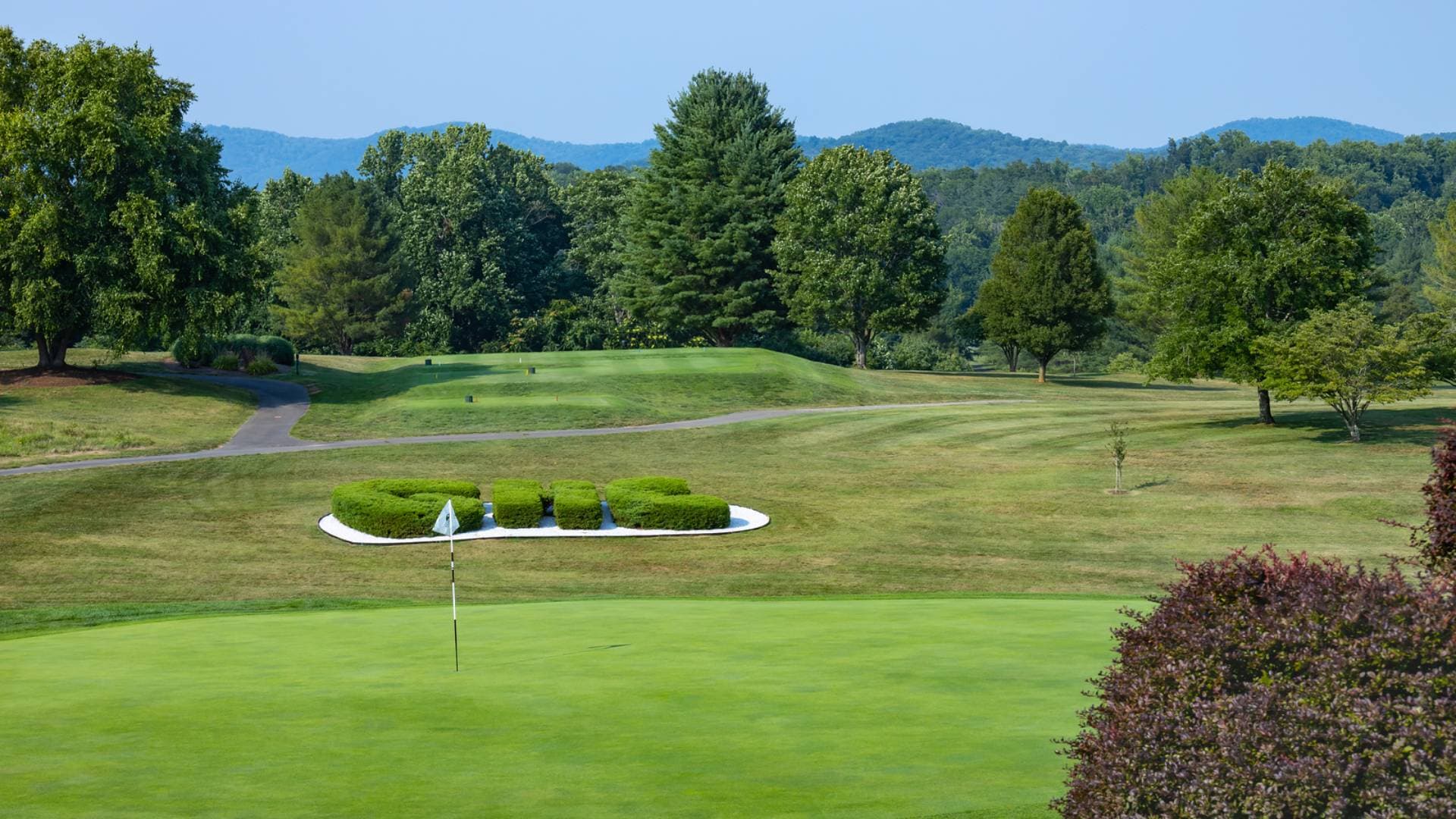 The signature green at Greene Hills, with a 'GHC' hedge topiary set into a bunker and the Blue Ridge Mountains rising behind.