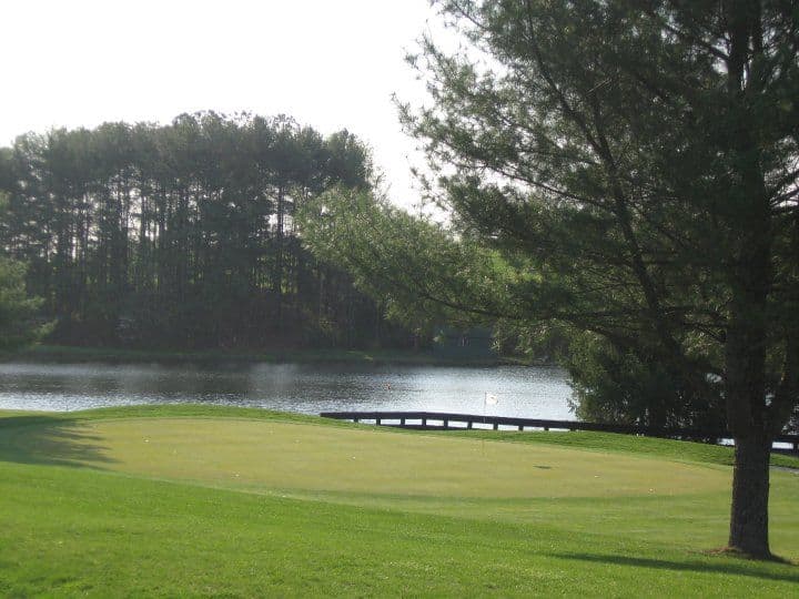 A Greene Hills green beside a quiet pond, framed by mature pines.
