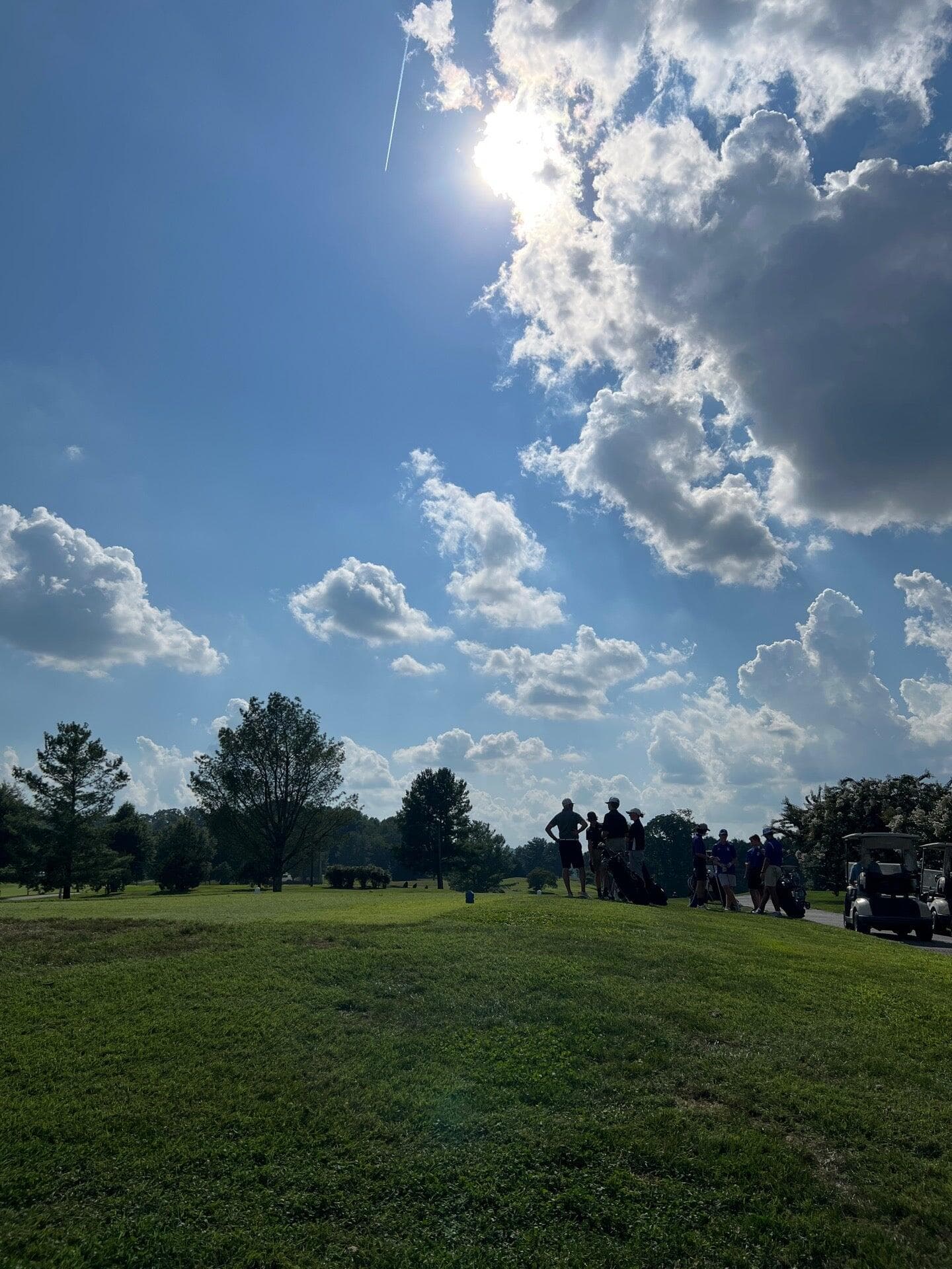 Junior golfers and golf carts on a Greene Hills fairway beneath a towering summer sky.