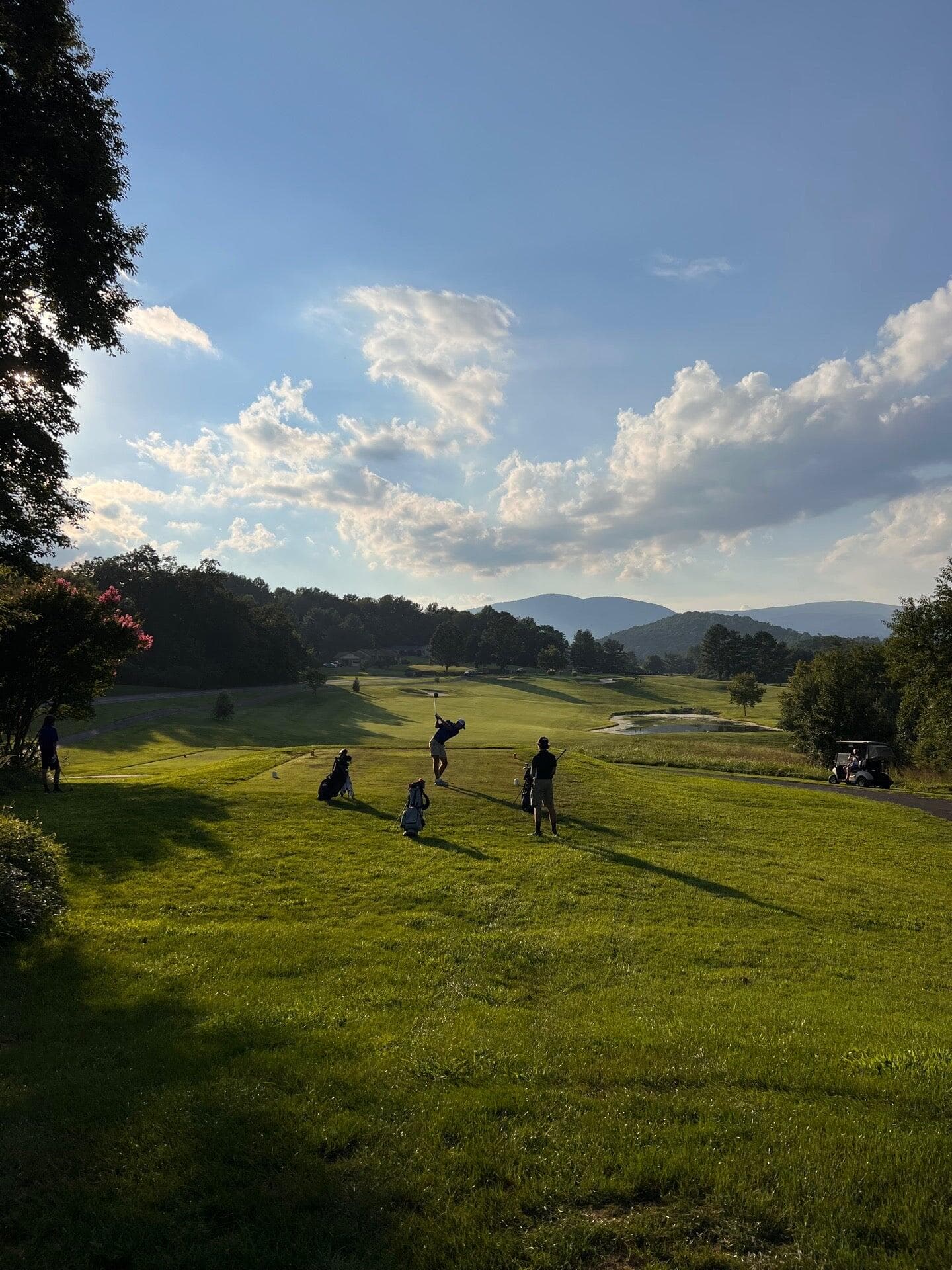 Two golfers walking up a Greene Hills fairway in late afternoon light, with the Blue Ridge ridgeline rising behind them.
